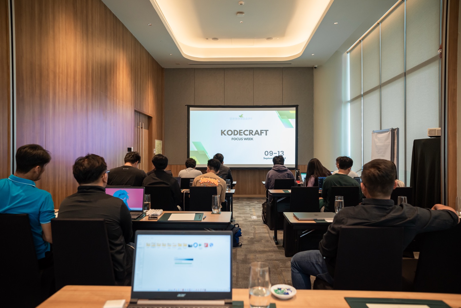Rows of laptops and teammates facing a projector in a meeting room