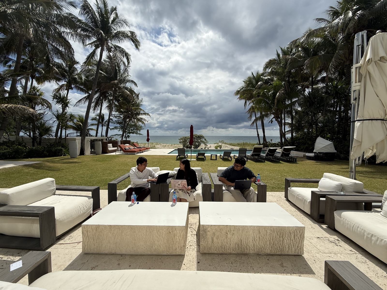 Three people meeting with laptops in an outdoor seating area by the ocean in Miami