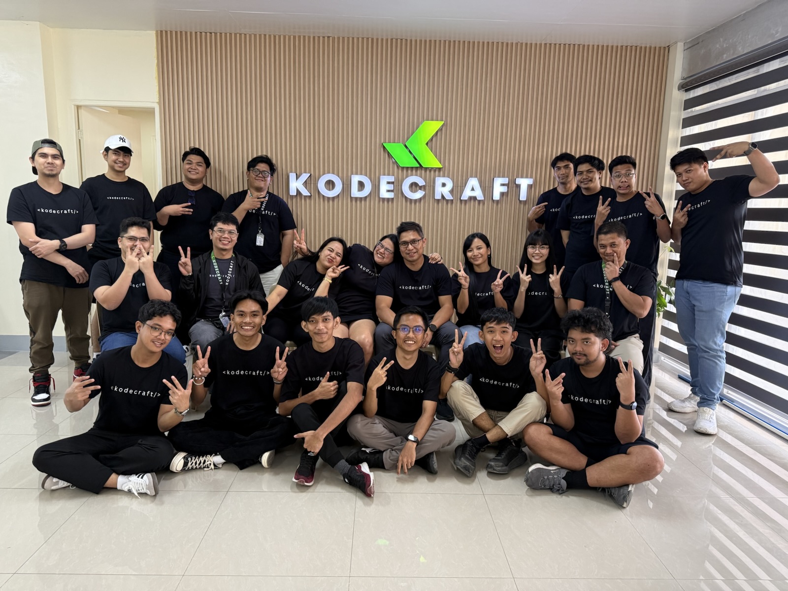 KodeCraft teammates smiling and making playful poses in front of the office sign